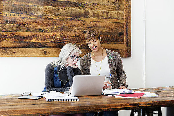 Weibliche Geschäftskolleginnen mit Laptop am Tisch im Kreativbüro