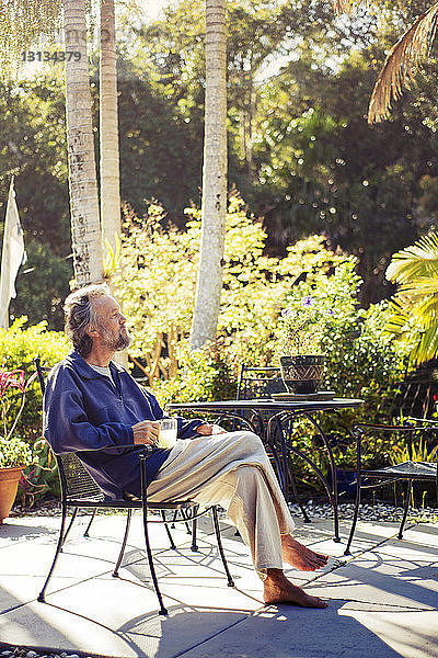 Nachdenklicher älterer Mann sitzt auf einem Stuhl im Hinterhof