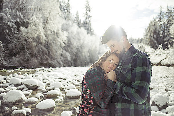Porträt einer Frau  die einen Mann umarmt  während sie im Wald im Lynn Canyon Park im Winter steht