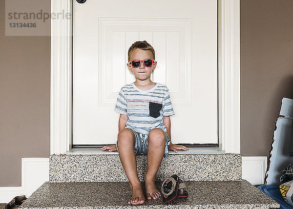 Junge in voller Länge mit Sonnenbrille auf Türrahmen sitzend