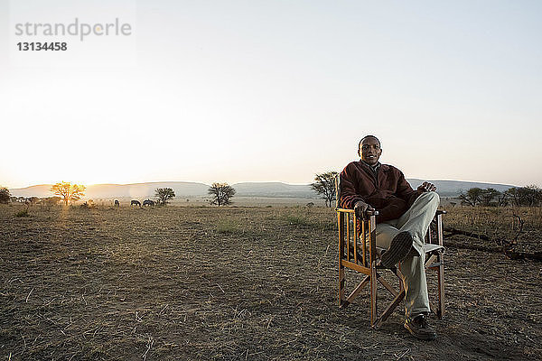 Porträt eines lächelnden Mannes auf einem Stuhl im Serengeti-Nationalpark vor klarem Himmel