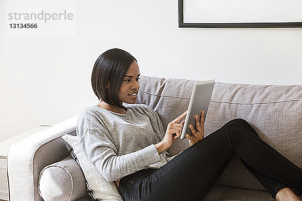 Frau benutzt Tablet-Computer auf dem Sofa zu Hause