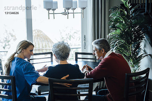 Hausangestellte diskutiert mit älterem Paar am Esstisch