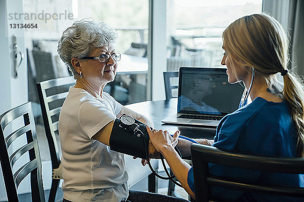 Häusliche Pflegekraft kontrolliert den Blutdruck einer älteren Frau am Esstisch