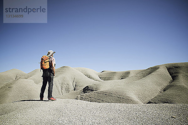 Rückansicht eines Rucksacktouristen  der auf Sand in der Wüste vor strahlend blauem Himmel steht