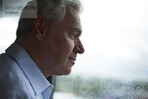 Lächelnder Mann schaut durch nasses Fenster  während er zu Hause steht