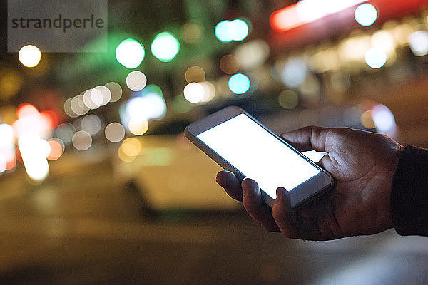 Abgetrennte Hand hält Smartphone in beleuchteter Stadt bei Nacht