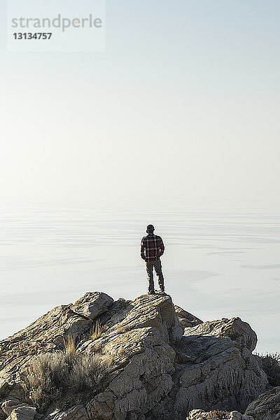 Rückansicht eines Menschen  der auf das Meer schaut  während er auf einem Felsen gegen den Himmel steht