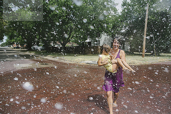 Verspielte Mutter  die ihre Tochter trägt  während sie sich am Springbrunnen erfreut