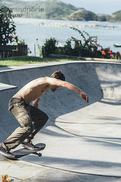 Seitenansicht eines hemdlosen jungen Mannes beim Skateboarden an der Sportrampe