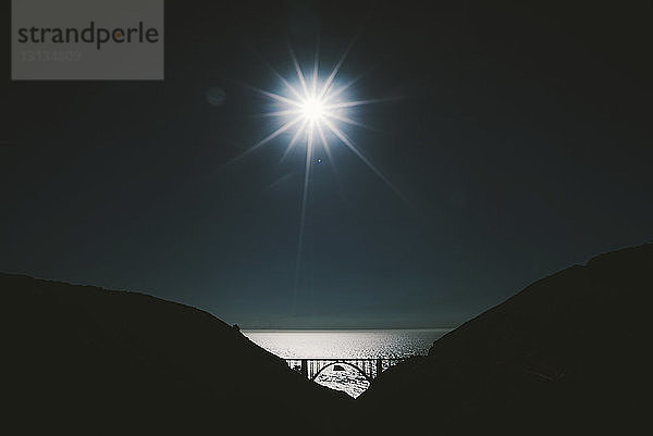 Strahlende Sonne über Meer und Silhouette des Berges