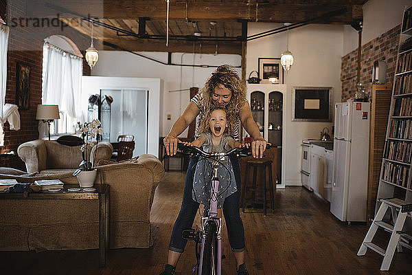 Glückliche Mutter mit Tochter fährt zu Hause Fahrrad