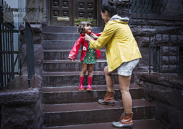 Mutter zieht der Tochter den Regenmantel auf der Treppe aus