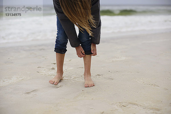 Mädchen rollt am Strand Jeans auf