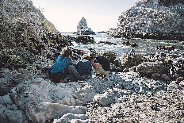 Freunde spielen  während sie auf Felsen am Strand kauern