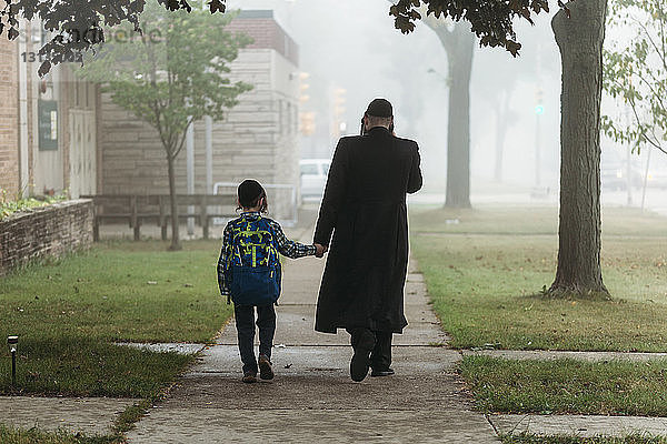 Rückansicht eines Vaters und eines Jungen  die bei nebligem Wetter auf einem Fußweg gehen