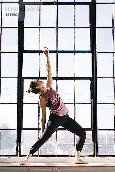 Weibliche Sportlerin praktiziert Yoga am Fenster in der Turnhalle