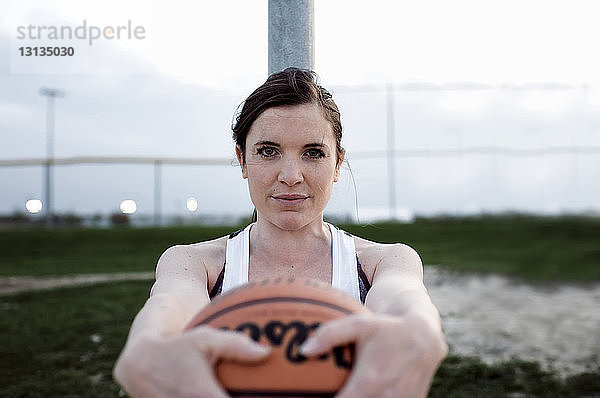 Porträt einer Frau  die den Basketball hält  während sie bei Sonnenuntergang an der Stange gegen den Himmel steht