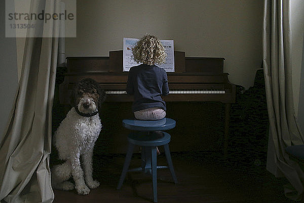 Junge sitzt neben einem Mädchen  das zu Hause Klavier spielt