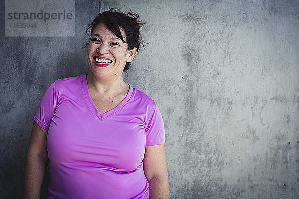 Porträt einer fröhlichen Frau  die im Yoga-Studio an der Wand steht
