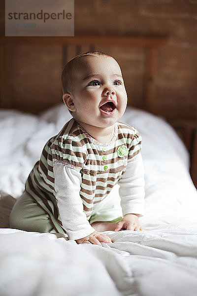 Süßes Baby-Mädchen schaut auf  während es zu Hause auf dem Bett kniet