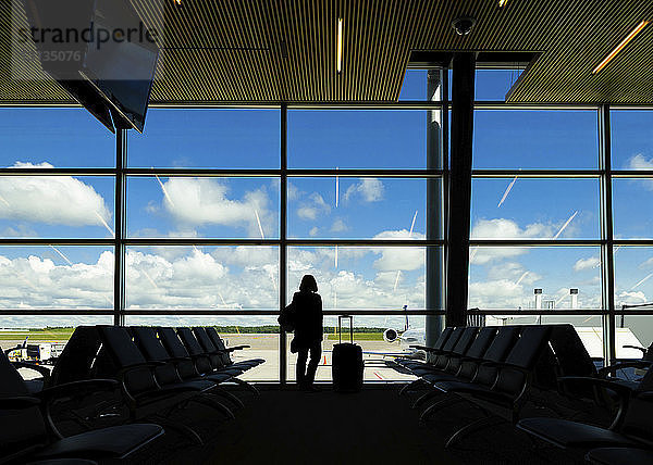 Silhouette einer Frau mit Koffer am Flughafen vor dem Fenster stehend