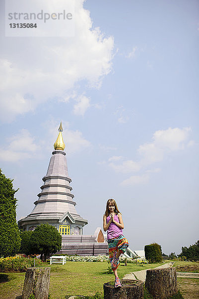 Mädchen steht in Baumpose vor Pagode im Doi-Inthanon-Nationalpark