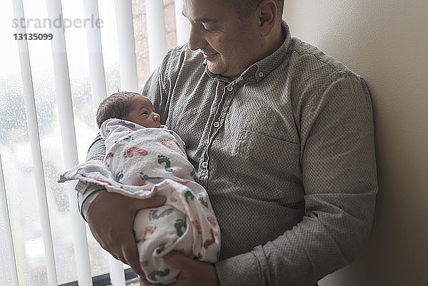 Vater trägt neugeborenen Sohn  während er im Krankenhaus am Fenster steht