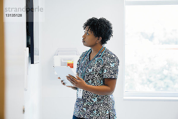 Ärztin schaut auf Flachbildschirm  während sie im Krankenhaus einen Tablet-Computer in der Hand hält