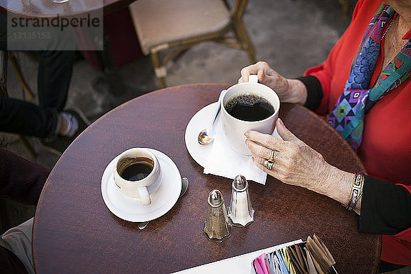 Mittelteil einer älteren Frau mit Kaffeetasse im Straßencafé