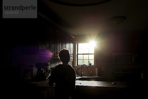 Scherenschnitt-Junge  der in der Küche stehend durch das Fenster in die Sonne schaut