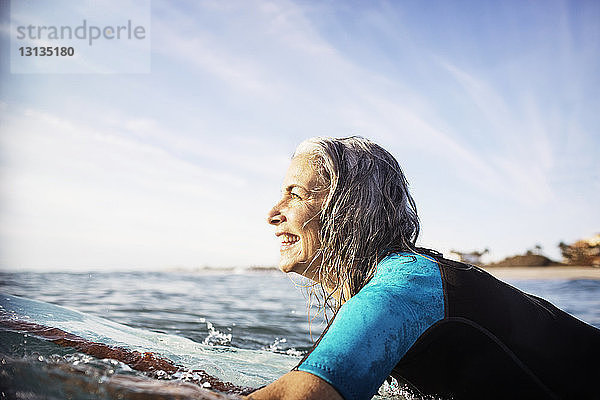 Seitenansicht einer glücklichen reifen Frau  die auf einem Surfbrett im Meer liegt