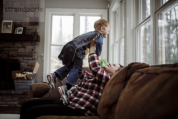 Glückliche Mutter holt Sohn ab  während sie zu Hause auf dem Sofa sitzt