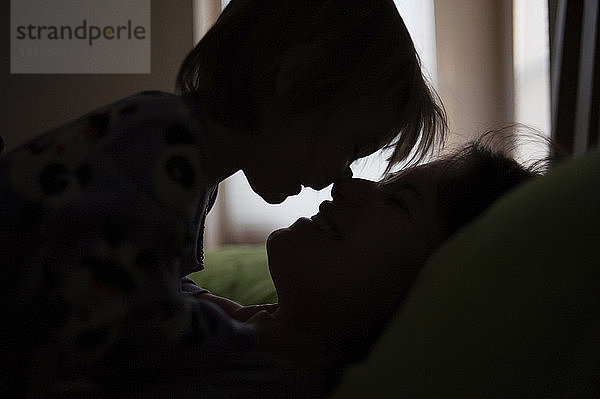 Scherenschnitt Mutter und Tochter reiben sich beim Entspannen zu Hause im Bett