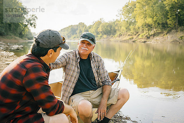 Männliche Freunde unterhalten sich  während sie auf einem Boot am See sitzen