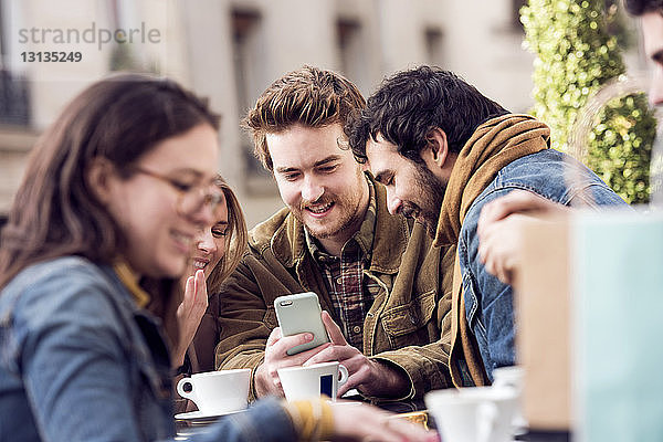 Glückliche Freunde benutzen gemeinsam ein Smartphone im Straßencafé