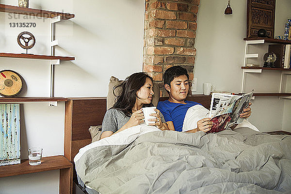 Ehemann und Ehefrau lesen Zeitschrift  während sie zu Hause im Bett liegen