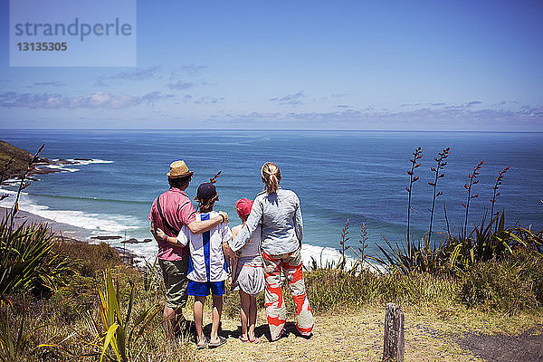 Rückansicht einer Familie  die auf einem Hügel steht und das Meer gegen den Himmel betrachtet