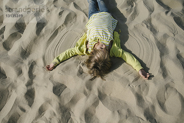 Draufsicht eines Mädchens  das am Strand einen Sandengel macht