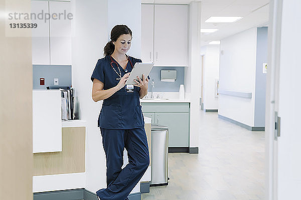 Ärztin  die einen Tablet-Computer benutzt  während sie sich im Krankenhaus an eine architektonische Säule lehnt