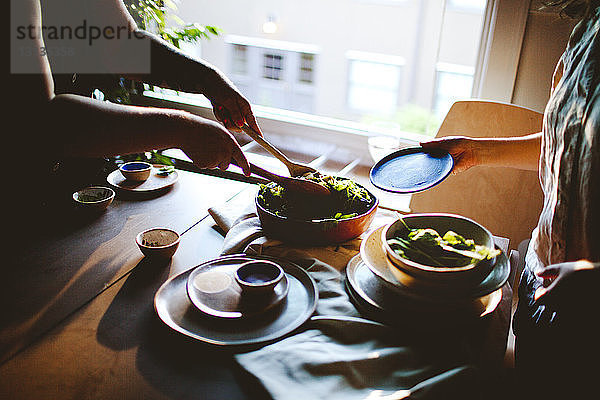 Ein Mann in der Mitte serviert frischen Salat für einen Freund am Esstisch