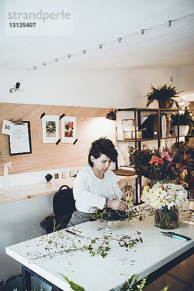 Florist arrangiert Blumen auf Blumenschaum bei Tisch im Laden