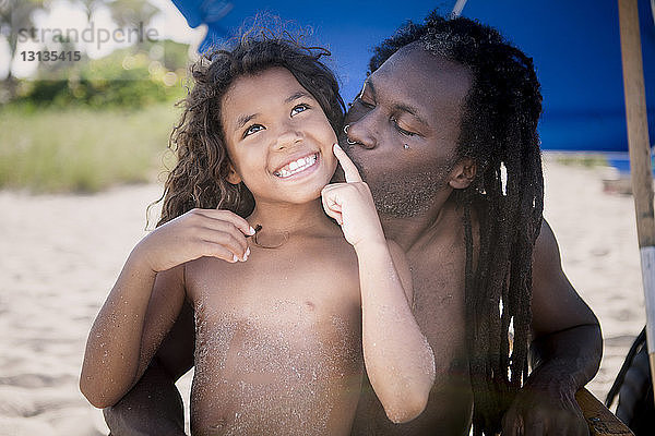 Vater küsst hemdlose fröhliche Tochter am Strand