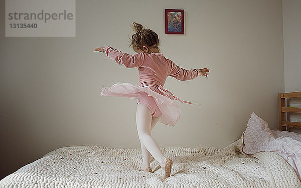 Mädchen in Ballettkostüm tanzt zu Hause auf dem Bett