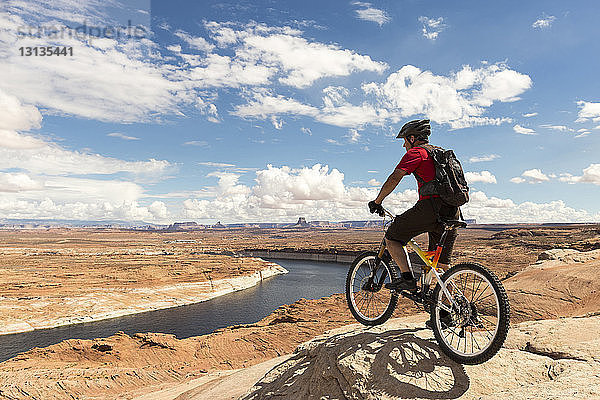 Mountainbiker mit Fahrrad auf Felsformation vor bewölktem Himmel stehend