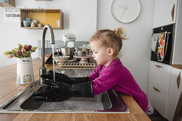 Mädchen mit Handschuhen beim Händewaschen in der Küchenspüle