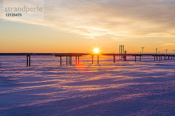 Pipeline auf schneebedecktem Feld gegen bewölkten Himmel bei Sonnenuntergang