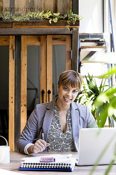 Porträt einer lächelnden  mittleren erwachsenen Geschäftsfrau  die am Schreibtisch einen Laptop benutzt