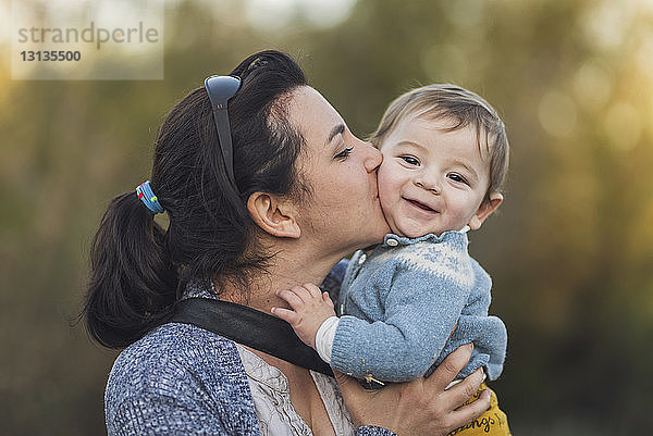 Nahaufnahme einer glücklichen Mutter  die ihren Sohn küsst  während sie an Bäumen steht