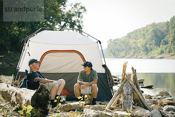 Freunde unterhalten sich beim Entspannen auf einem Campingplatz am See gegen den Himmel
